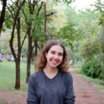 Young woman smiling brightly in a green park setting during daytime.