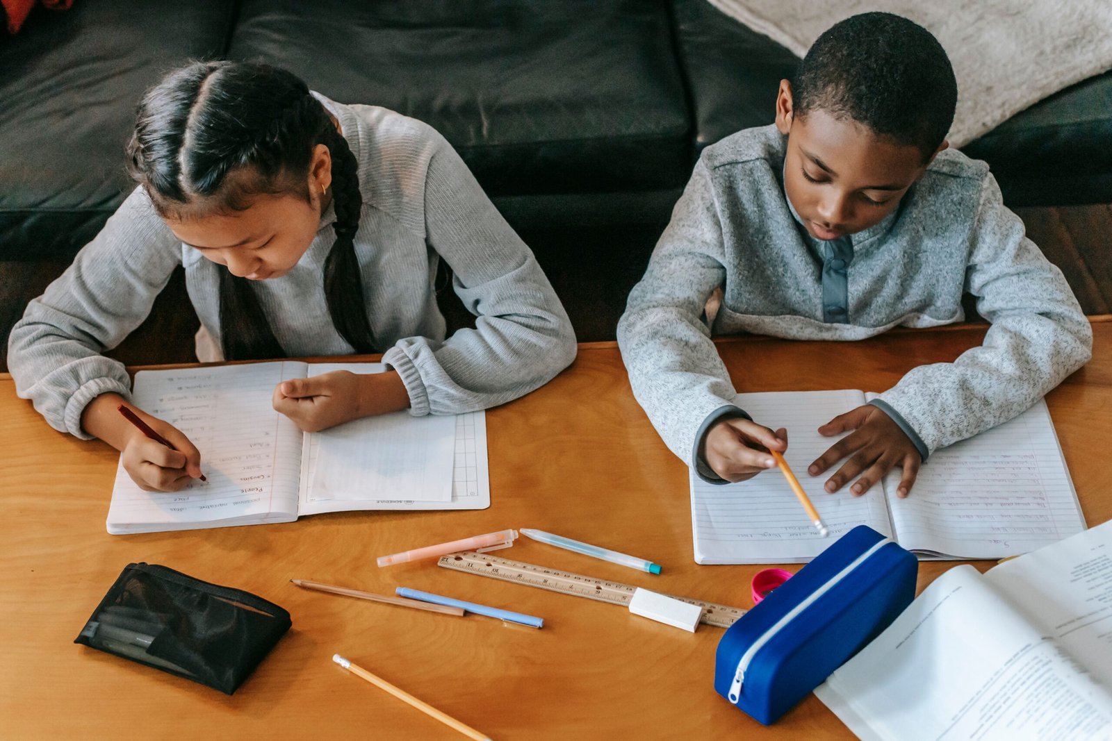 From above of concentrated multiracial kids doing homework assignments together sitting at wooden table