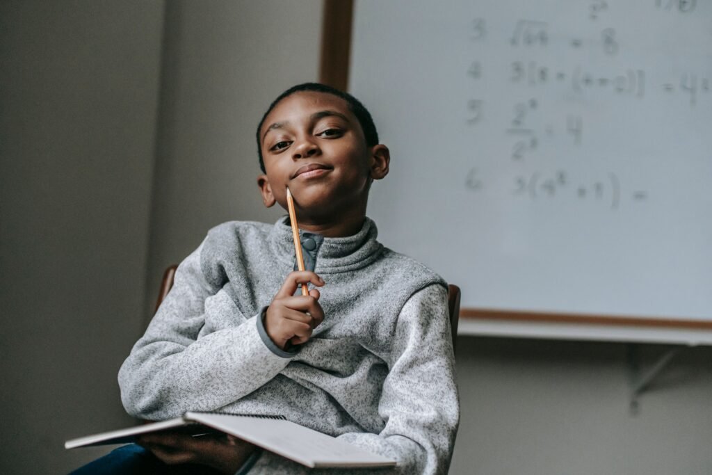 Pensive African American boy with pencil and copybook sitting on chair at school and writing
