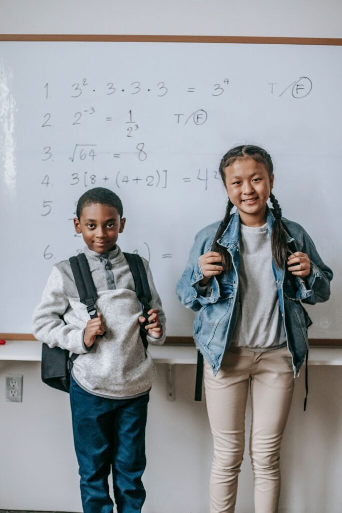 Glad multiethnic classmates with school bags looking at camera after math lesson in daylight