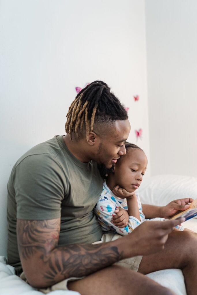 Father and child share a bonding moment reading a book on a cozy bed in a bright room.