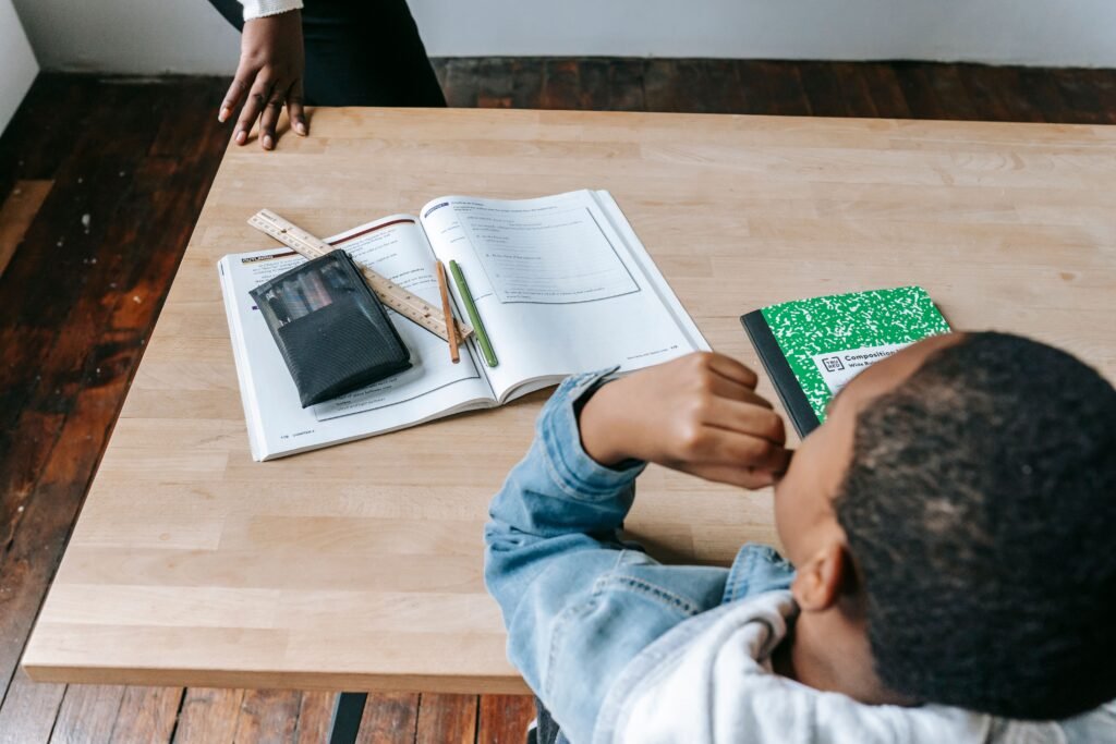 Crop unrecognizable schoolboy with textbook and pencils sitting at table in modern classroom
