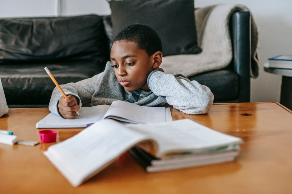 Focused African American boy writing in copybook with pencil while doing homework at wooden table