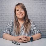 Cheerful female with crossed hands looking at camera while sitting at white table against brick wall